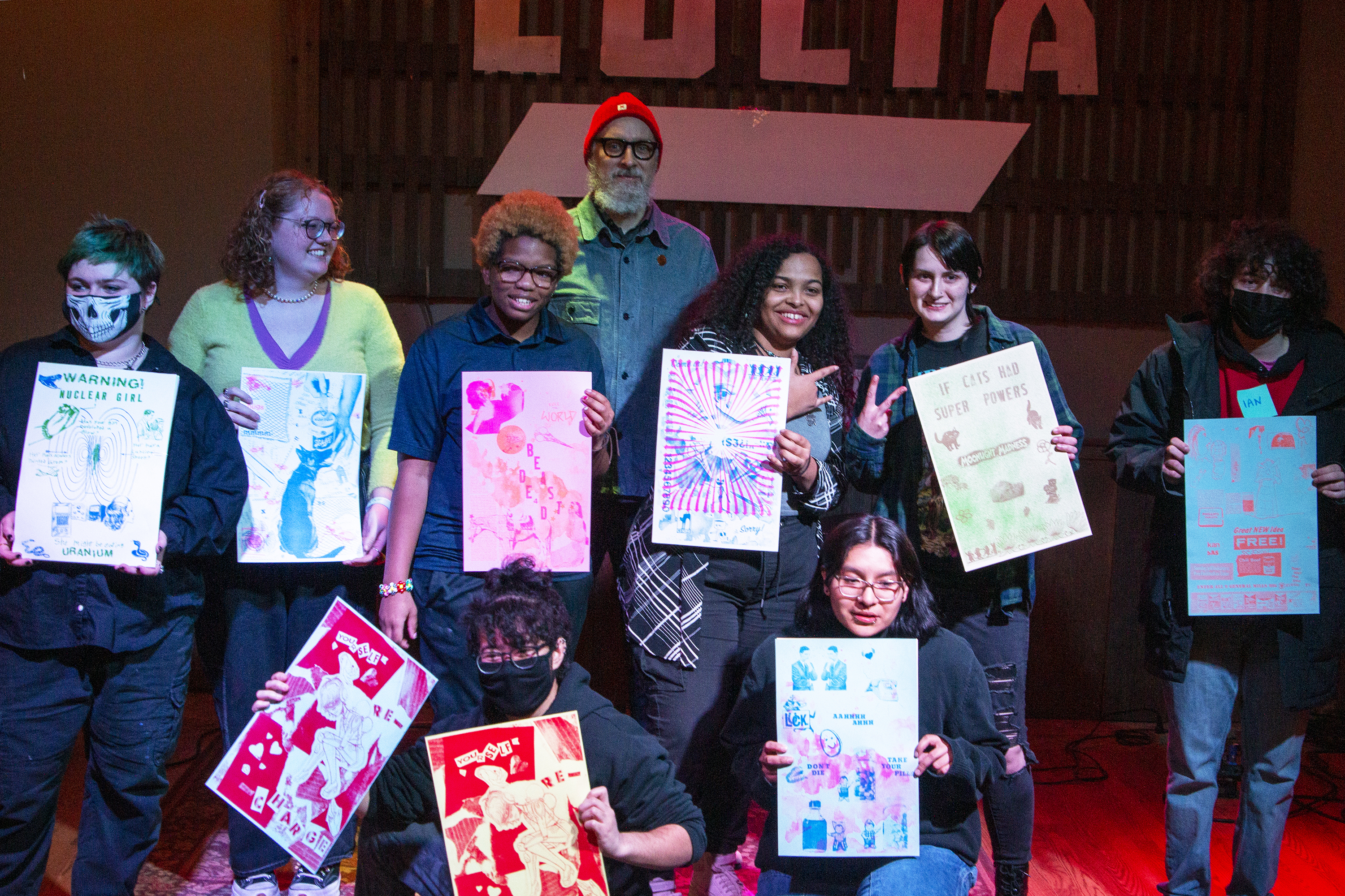 Ryan D. Clifford, Assistant Professor of Design and Visual Communication on stage with participants of the Radlab! workshop, all holding up their risographic art creations.